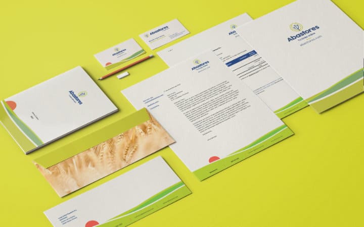Corporate stationery of Abastores highlighting its symbolic sunrise made in flat vector graphics with a green field in various shades and the red sun of the sunrise.