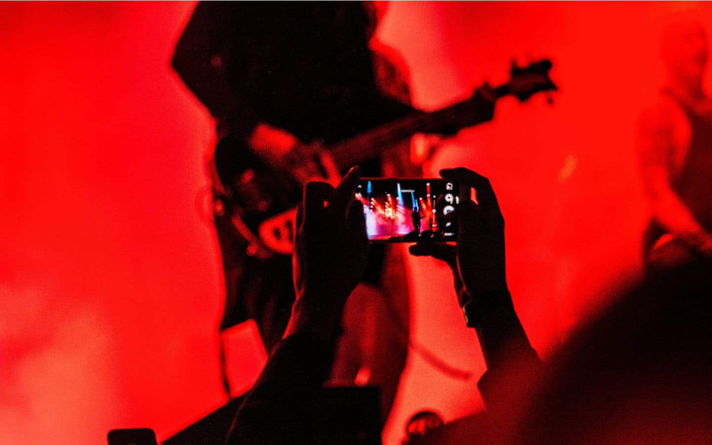 Hand holding a mobile phone at the concert, with red lights in the background.