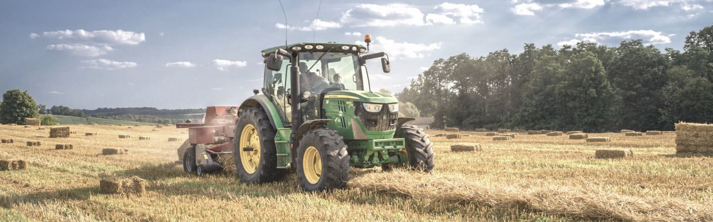 Tractor John Deere verde y amarillo recolectando pasto para animales en un campo abierto durante el día
