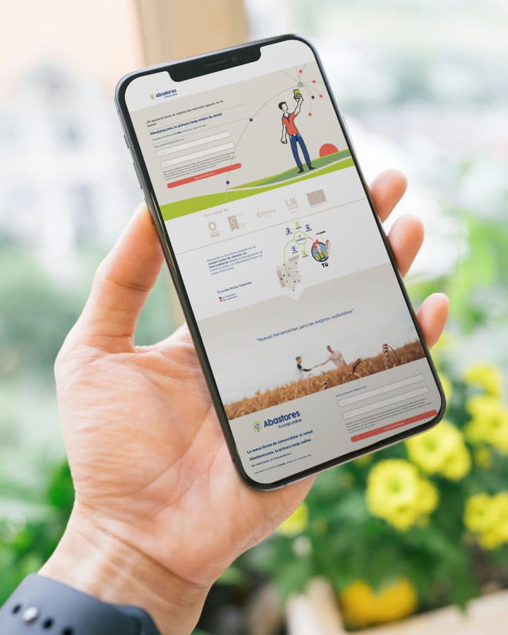 Mano de una persona aguantando un móvil en el que aparece la web de Abastores con formularios, explicación sobre la empresa y la identidad visual de la marca. En el fondo hay plantas y tonos verdosos relacionados con Abastores.
